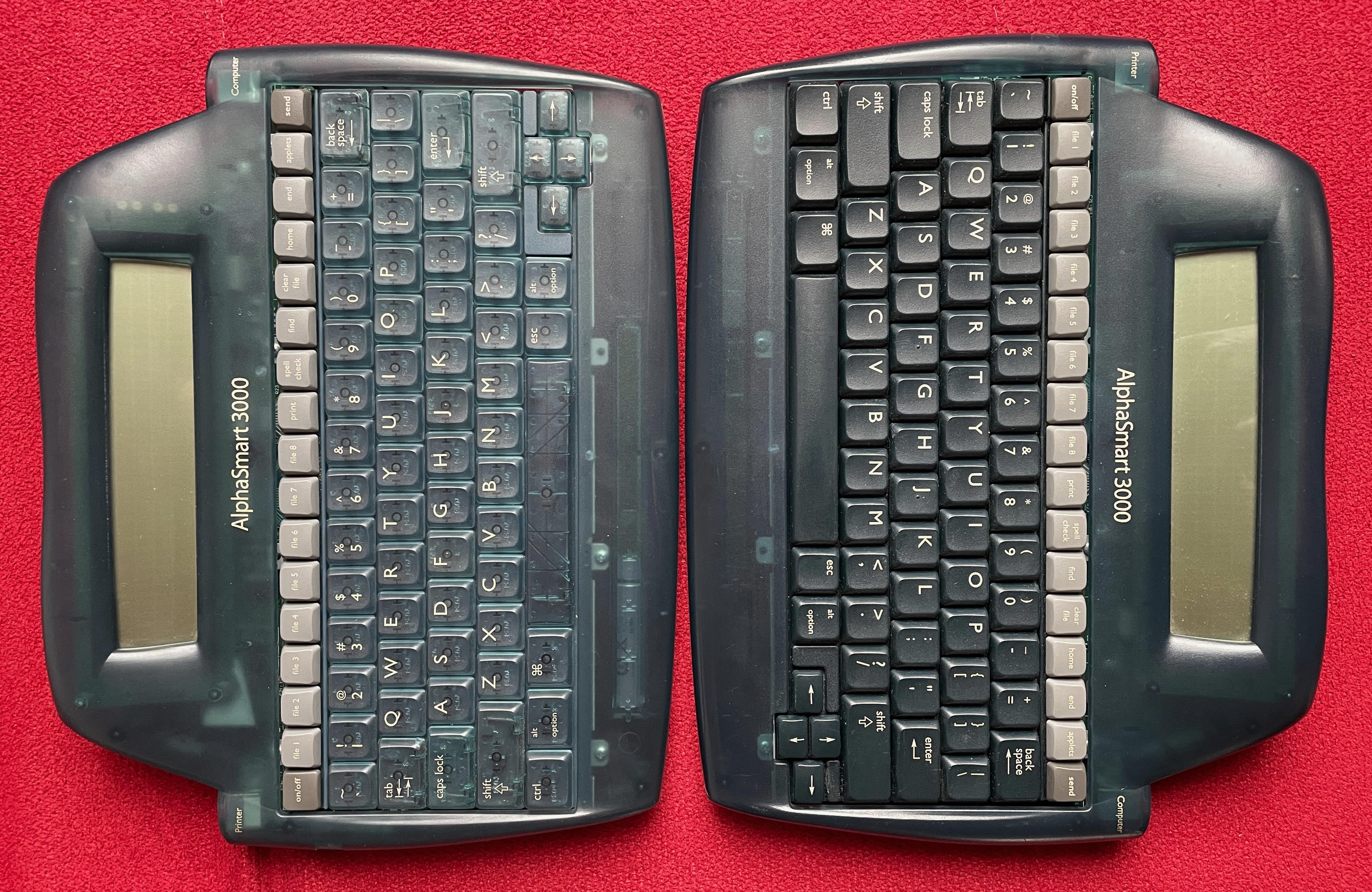 Two AlphaSmart 3000 devices on a red background. You can see the differences between the keyboards and the casing, as described in the text.